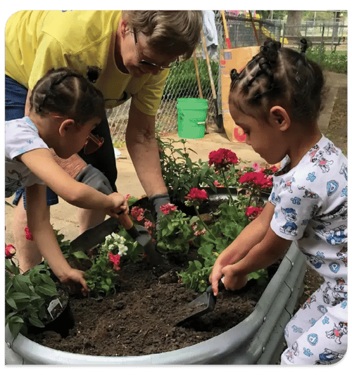 A adult and two children planting flowers in a planter A adult and two children planting flowers in a planter