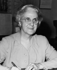 black and white picture of a woman seated at a desk smiling at the camera