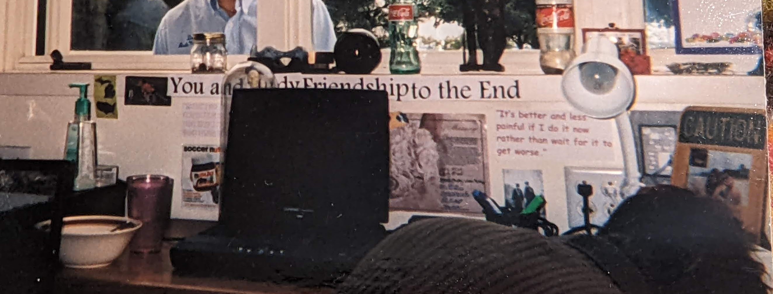 Picture of a desk and the wall behind the desk is covered with posters, snapshots, and other paraphanalia. The poster at center says "You and Study Hour: A Friendship to the End"