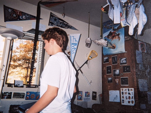 Picture of Emily standing in her dorm room, which is plastered with posters, snapshots, sport equipment, and other paraphernalia. 